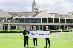 Three men stand on a golf course holding a large sponsor sign with logos for PGA, elavon, and MCM, in front of a clubhouse clock tower.