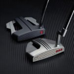 Two golf clubs resting on a dark textured surface, highlighting metallic club heads and shafts.