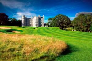 Castle-like stone building on a lush golf course under a bright blue sky with trees surrounding the grounds