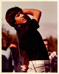 Screenshot - Talk Golf Ireland - Talk Golf Ireland Man mid-swing playing golf, wearing a dark shirt and light plaid pants with spectators in the background.
