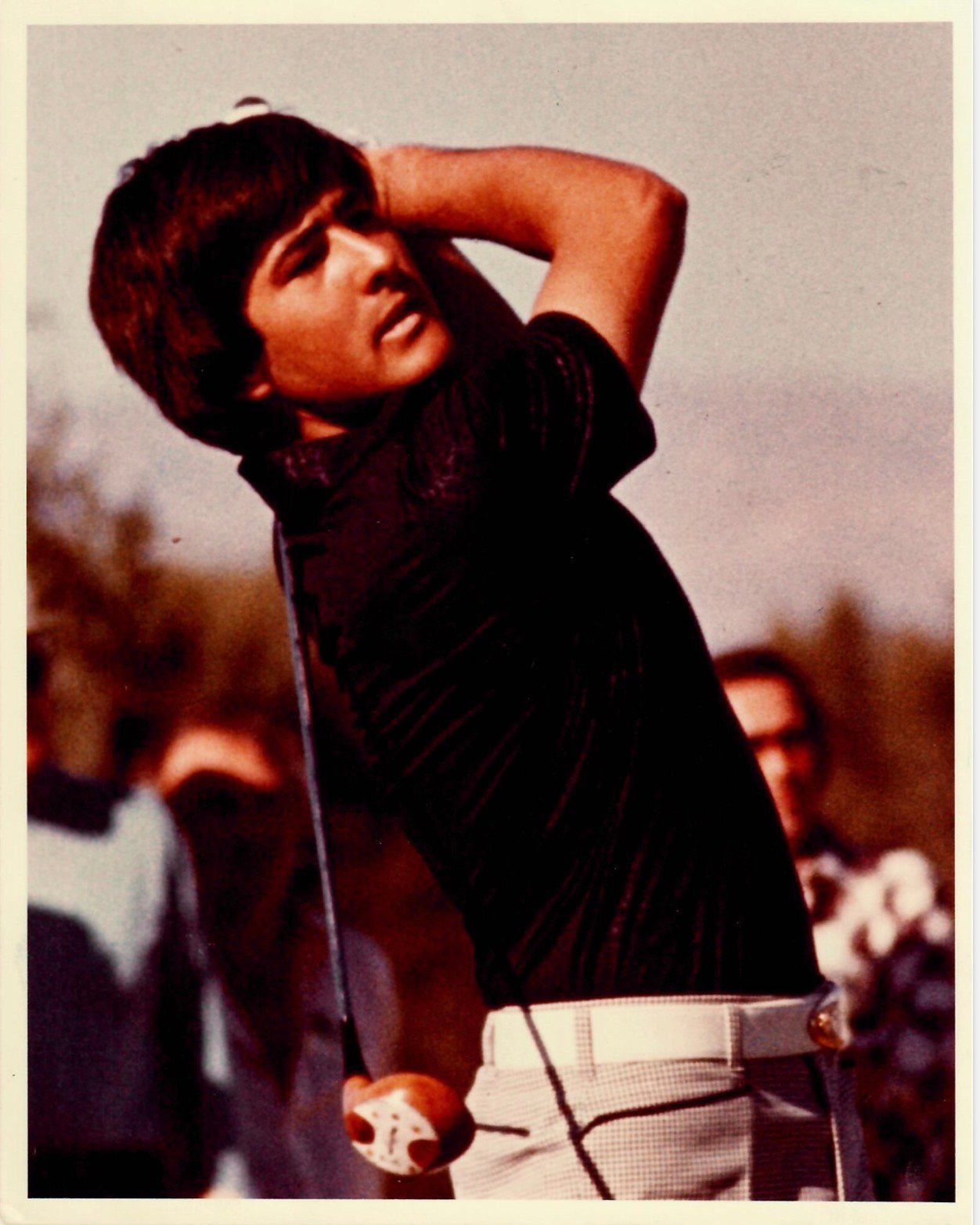 Screenshot - Talk Golf Ireland - Talk Golf Ireland Man mid-swing playing golf, wearing a dark shirt and light plaid pants with spectators in the background.