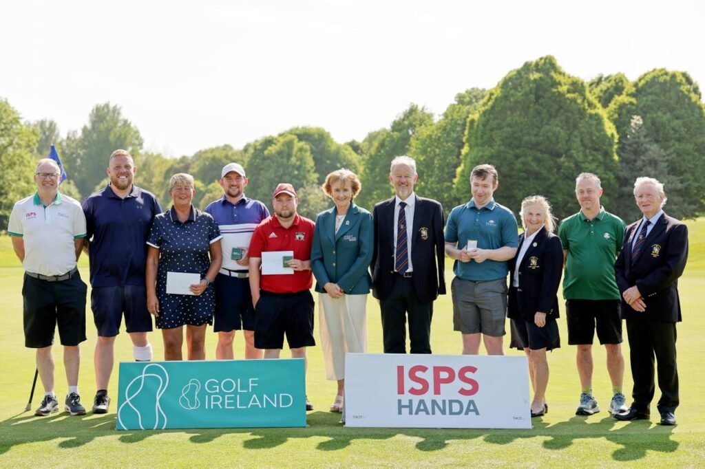 Group of golfers standing on a golf course with prize envelopes, banners reading 'Golf Ireland' and 'ISPS Handa' in front.