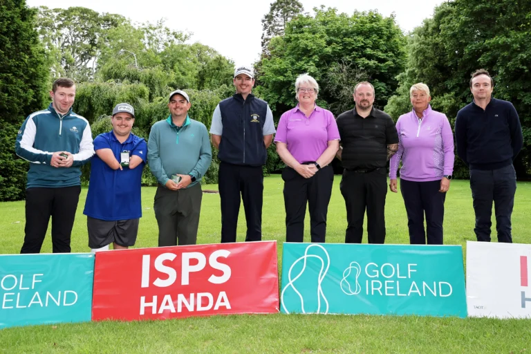 Eight people stand in a line on a golf course, posing for a group photo with colorful sponsor banners in front.