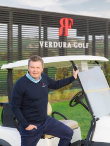 The Simon Holmes Golf Academy3 002 - Talk Golf Ireland Man in a navy sweater seated in a white golf cart with Verdura Golf branding visible in the background