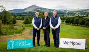 - Talk Golf Ireland Three men in navy vests stand together on a golf course with hills in the background and sponsor signs in the foreground.