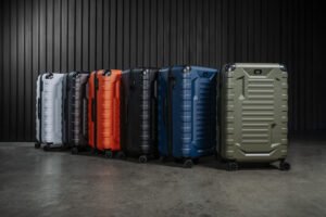 Row of colorful hard-shell suitcases on wheels lined up against a dark vertical-panel wall in a studio setting
