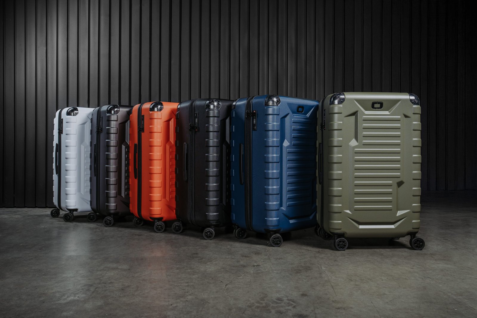 OGIOVault 002 - Talk Golf Ireland Row of colorful hard-shell suitcases on wheels lined up against a dark vertical-panel wall in a studio setting