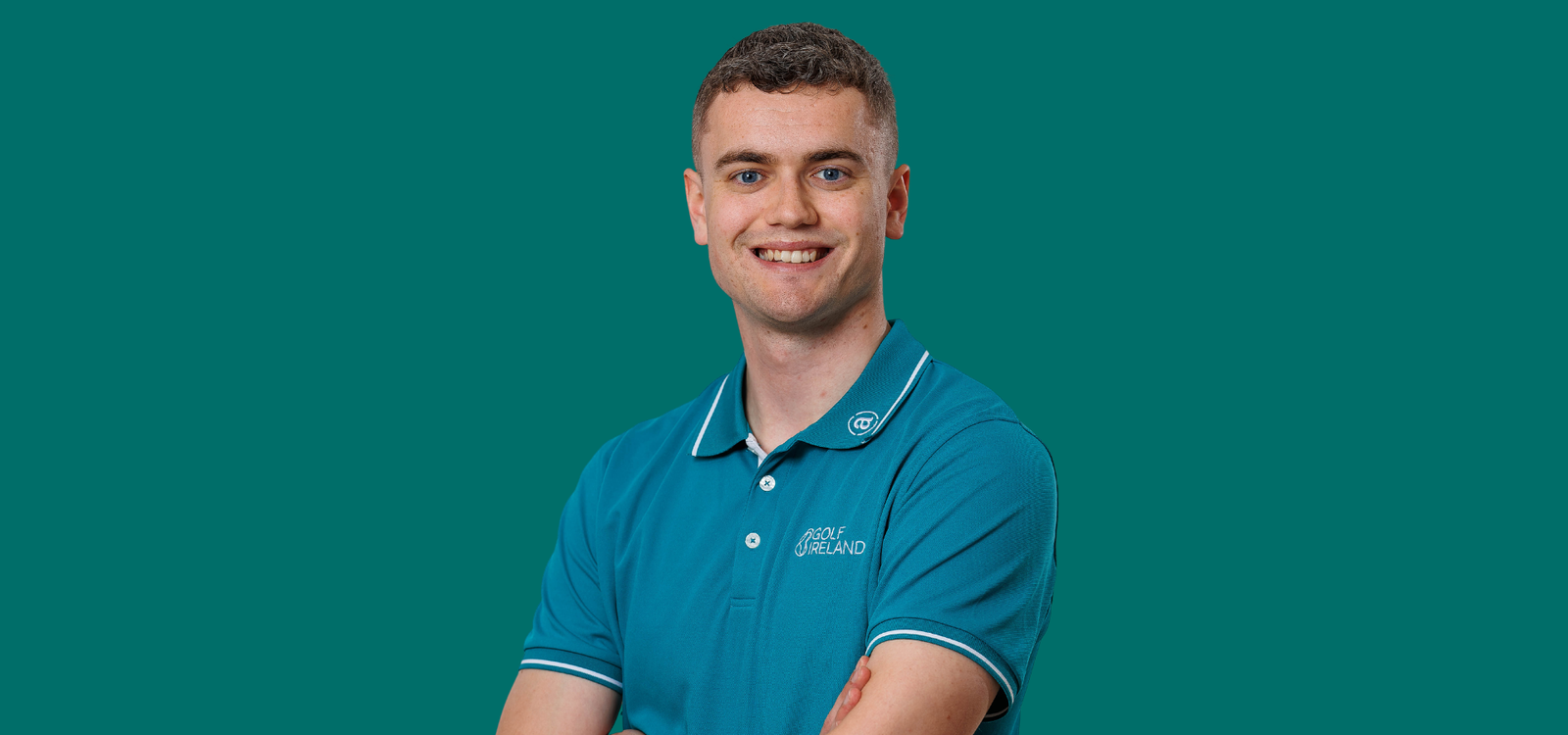 Ronan Murray - Talk Golf Ireland Portrait of a smiling man in a teal polo shirt with the Golf Ireland logo, arms crossed against a teal background.