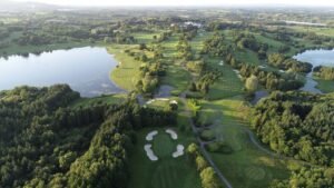 Slieve Russell - Talk Golf Ireland Aerial view of a large golf course with winding fairways, sand bunkers, and several water hazards surrounded by trees and a lake on the left side; distant landscape in the background.