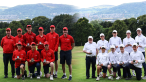 Group photo of a golf club team on a fairway, left in red uniforms and right in white uniforms, each member holding medals.