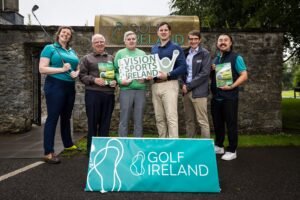 Group of six adults posing outdoors behind a turquoise Golf Ireland sign, holding golf brochures and a Vision Sports Ireland sign.