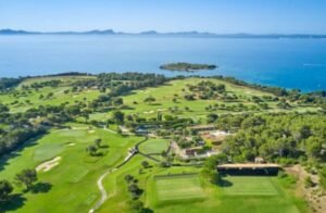 Aerial view of a coastal golf course with green fairways, sand bunkers, and a blue sea in the background near a small island.