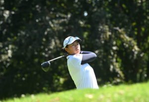 Anna Huang - Talk Golf Ireland Female golfer in a white shirt and cap mid-swing on a sunny golf course.