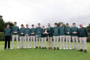 Young golf team in green sweaters and beige pants pose on a course, holding medals and a trophy ceremony photo.