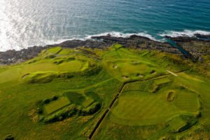 Course-Drone-4th-Green-5th-web - Talk Golf Ireland Aerial view of a coastal golf course with greens, bunkers, and a rocky shoreline.