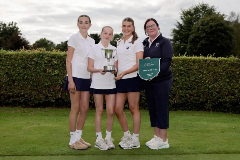 Four young female golfers pose on a green with a silver trophy and a Golf Ireland winner banner nearby.