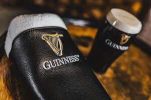 Close-up of a black leather glove with a Guinness logo and white cuff on a wooden surface]