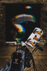 Golf bag with Guinness branding and a white toucan headcover, set against a rainbow mural in the background.